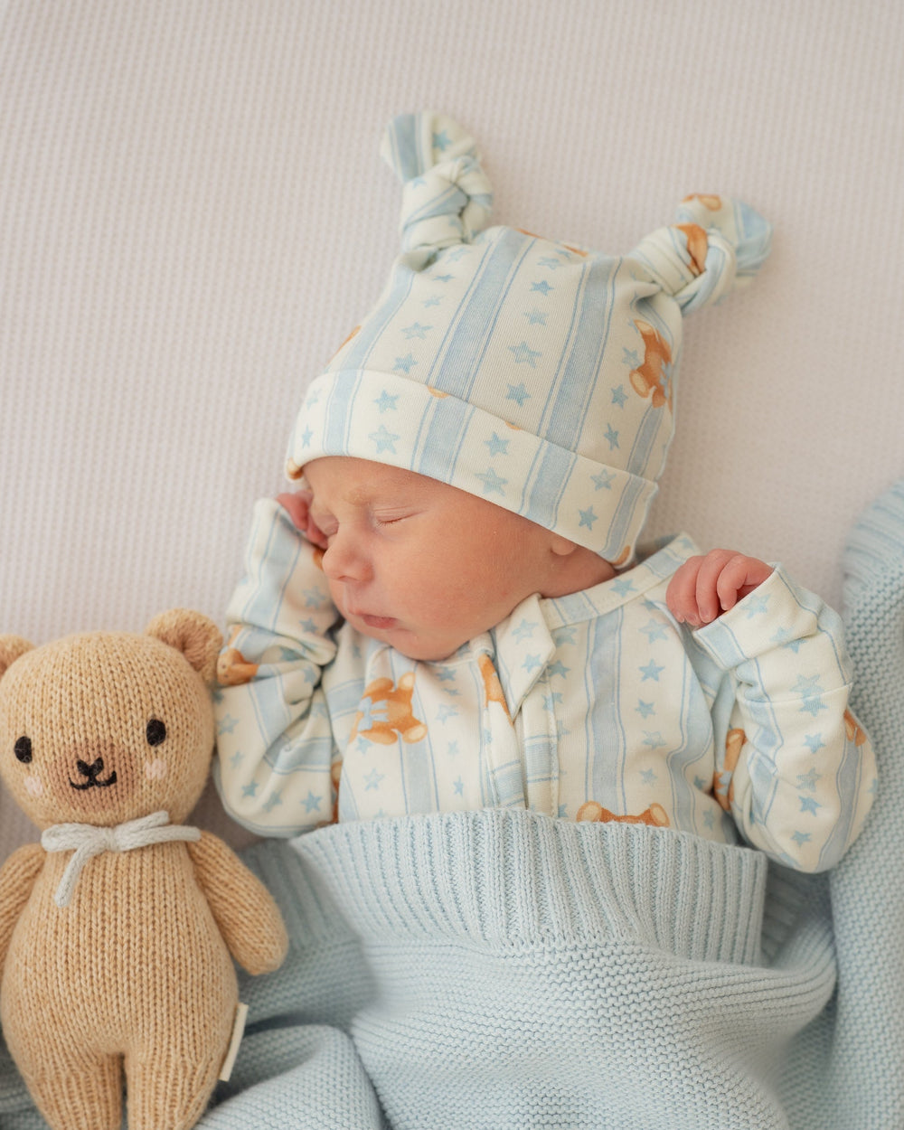 Newborn baby sleeping with a teddy bear and wearing a striped hat and outfit.