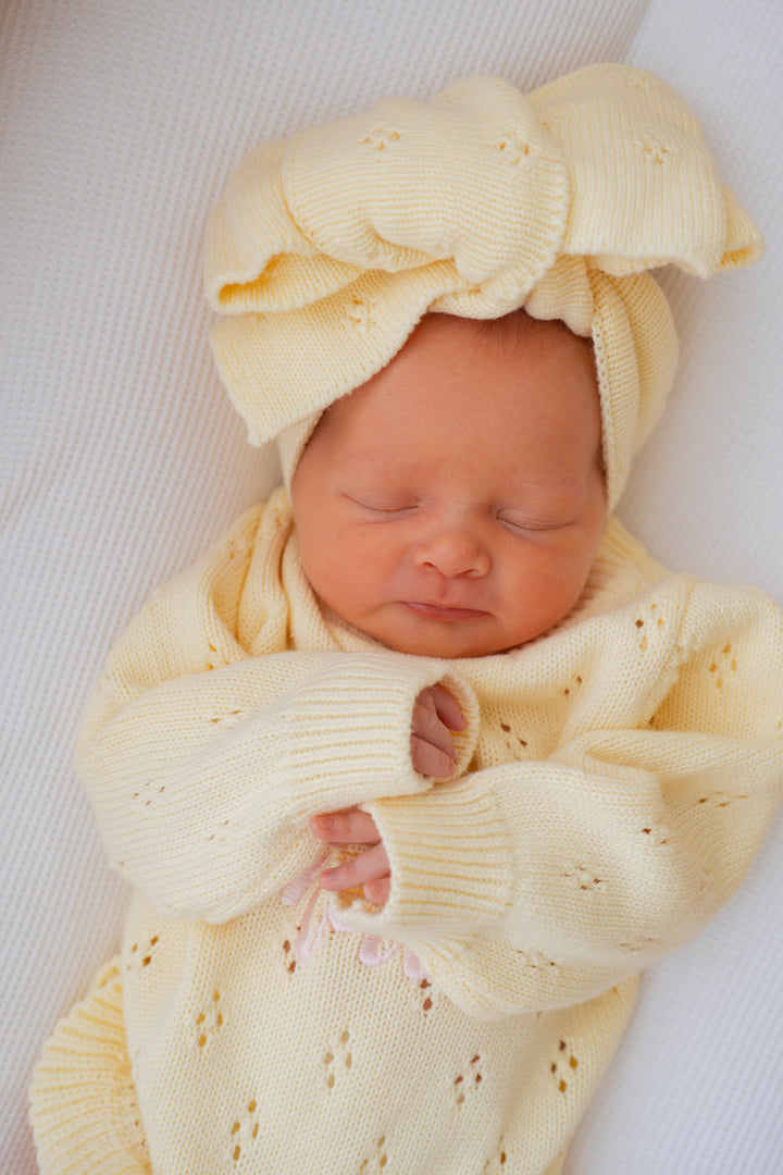 Newborn baby wrapped in a yellow knitted outfit with matching hat on a white background